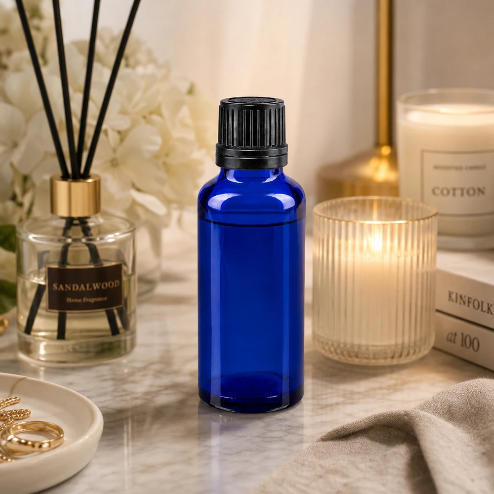 Apteekkipullo sininen 30ml ruuvikorkki musta valurengas sinetöintiturvallinen sulkeminen Sininen 30 ml:n lasipullo, jossa on musta tippakorkki, marmoripinnalla tuoksukynttilän ja huonetuoksun vieressä