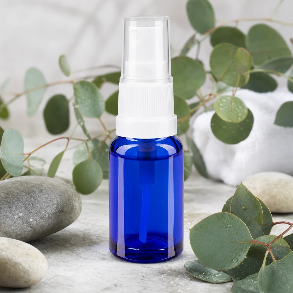 Apteekkipullo sininen 10ml ruiskukorkki valkoinen 10 ml:n pullo koboltinsinisestä apteekkilasista, jossa on valkoinen sumutinpää ja jota ympäröivät eukalyptusoksat