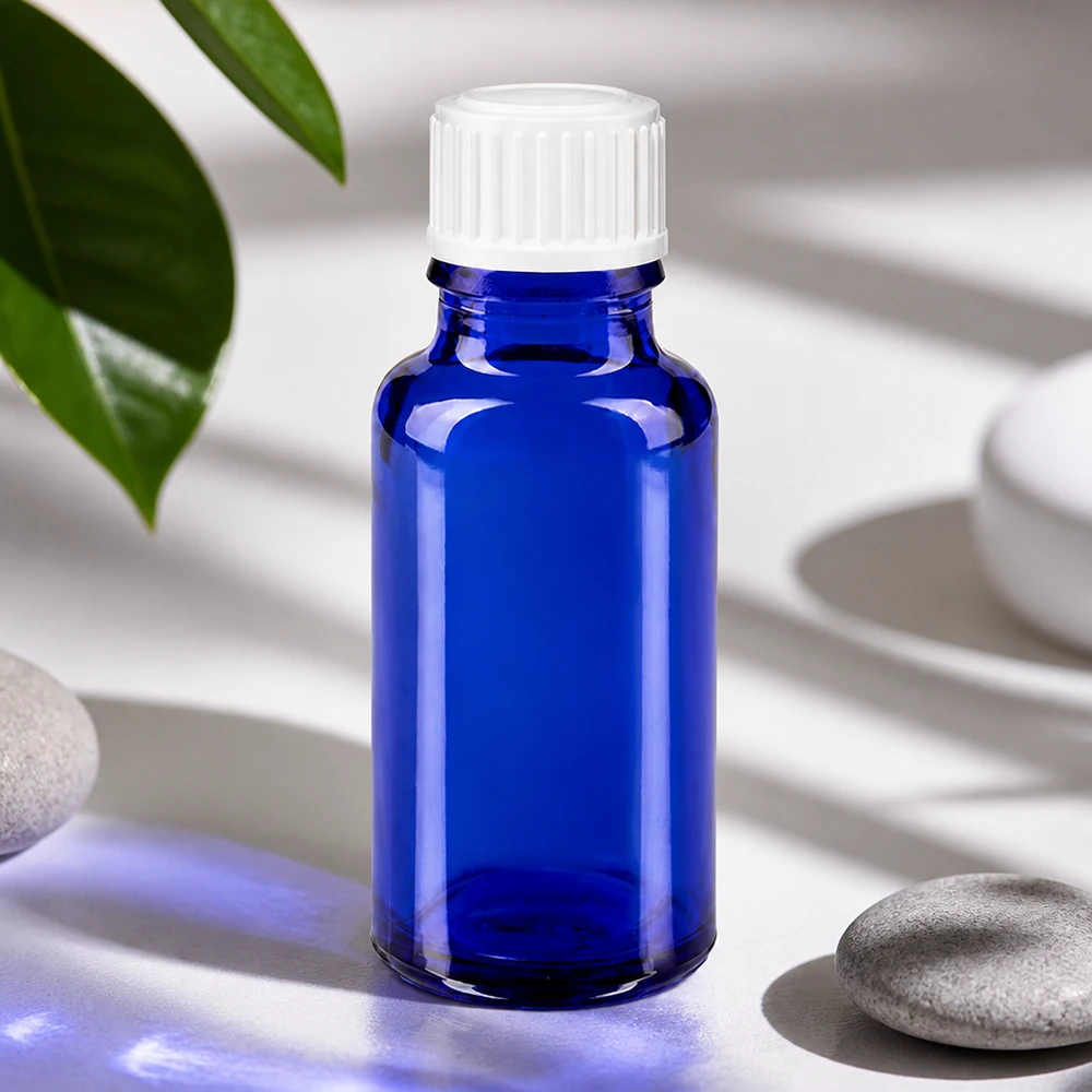 Apteekkipullo sininen 20ml ruuvikorkki valkoinen standardi Sininen 20 ml:n lasipullo, jossa on valkoinen korkki, luonnonkivien ja vihreiden lehtien vieressä