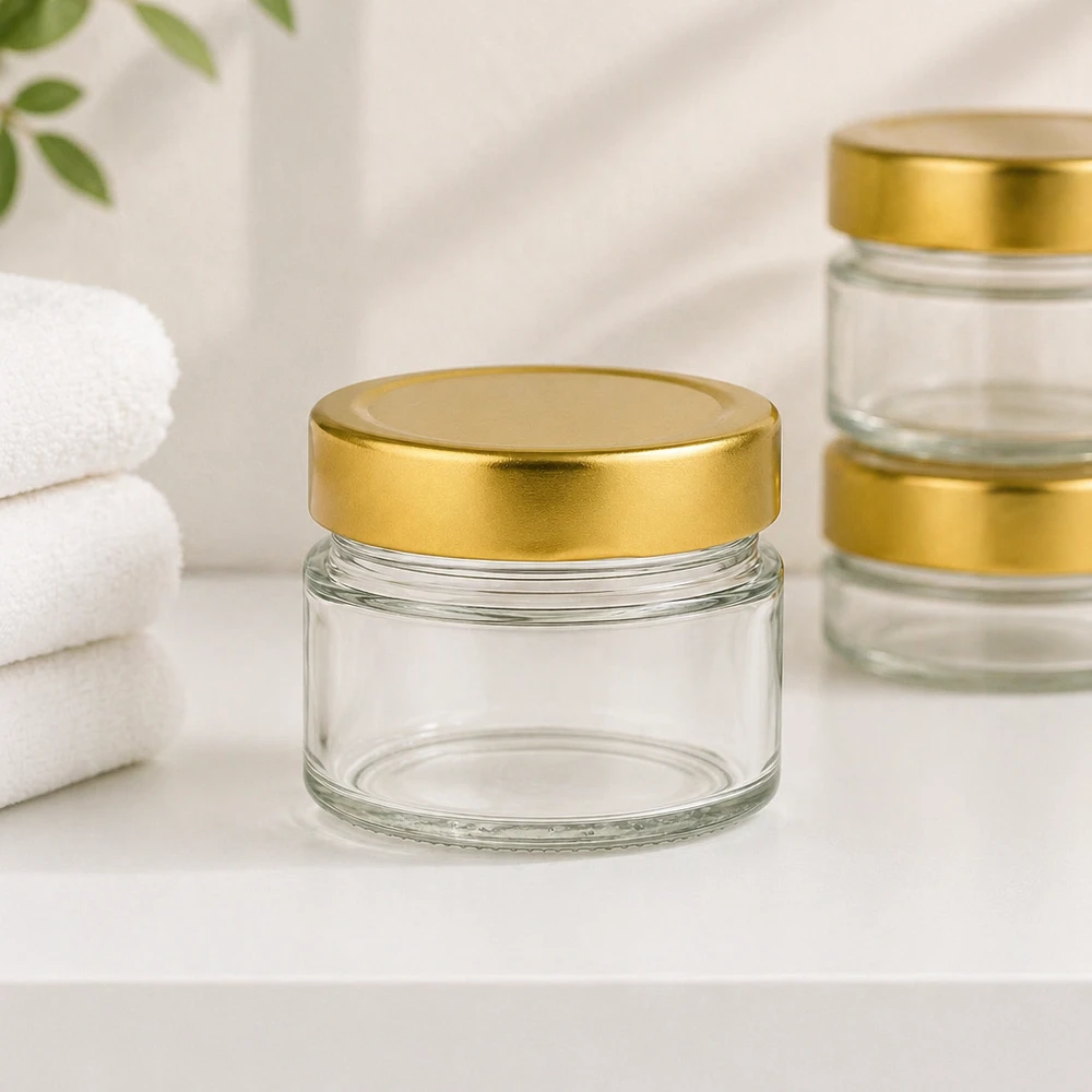 80ml pyöreä lasipurkki, jossa on BasicSeal-kansi kultainen syvä UNiTWIST 80ml pyöreä purkki, jossa on BasicSeal-kansi kultainen syvällä kylpyhuoneen tunnelmassa valkoisilla pyyhkeillä kosmetiikkaa varten.