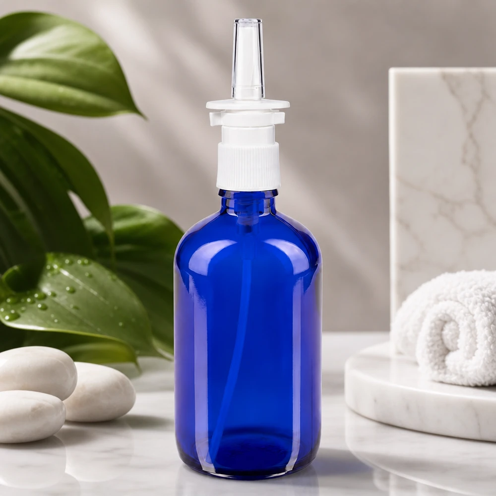 Koboltinsininen 100 ml:n lasipullo, jossa on nenäsumutinsuutin, valkoisella marmorilla wellness-kivien vieressä