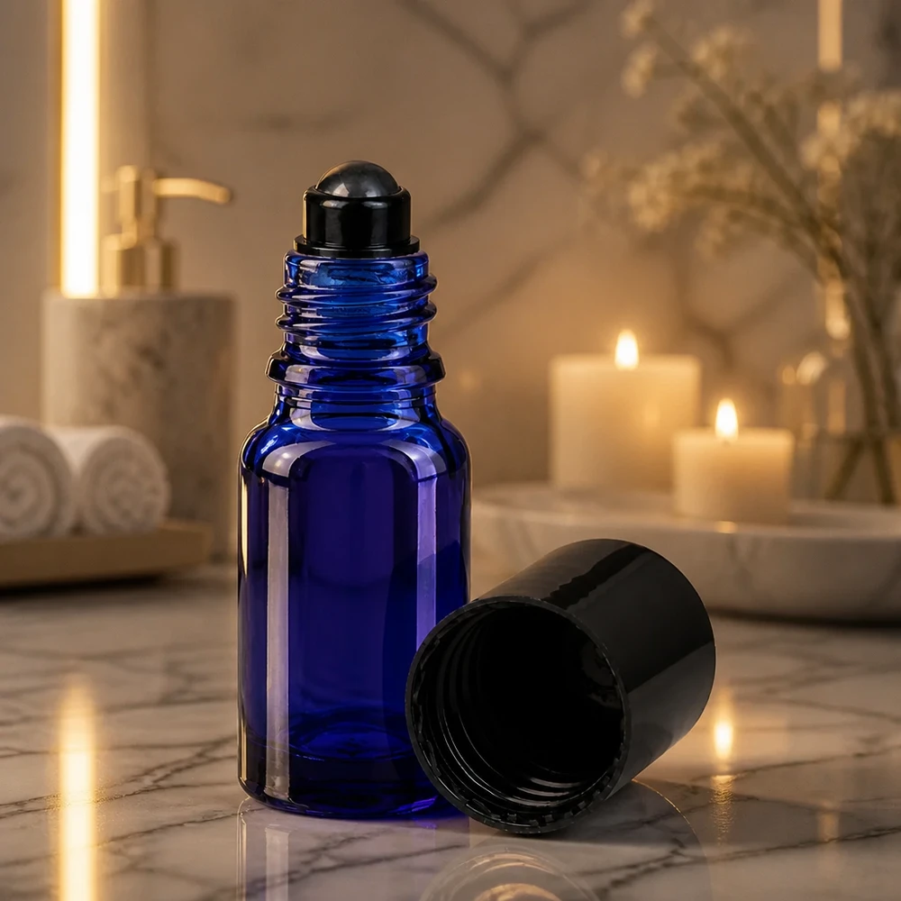 Apteekkipullo sininen 10ml roll-on korkki musta Koboltinsininen 10 ml:n roll-on-pullo, jossa on musta rullapallo, tunnelmallisessa kynttilänvalossa marmoripinnalla