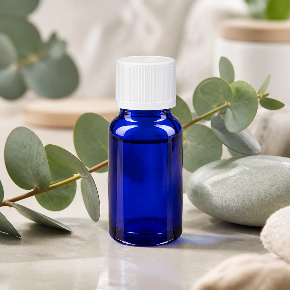 Apteekkipullo sininen 10ml tippapullon korkki valkoinen lapsiturvallinen standardi Koboltinsininen 10 ml:n apteekkipullo, jossa on valkoinen KiSi-korkki, eukalyptusoksien edessä marmorilla