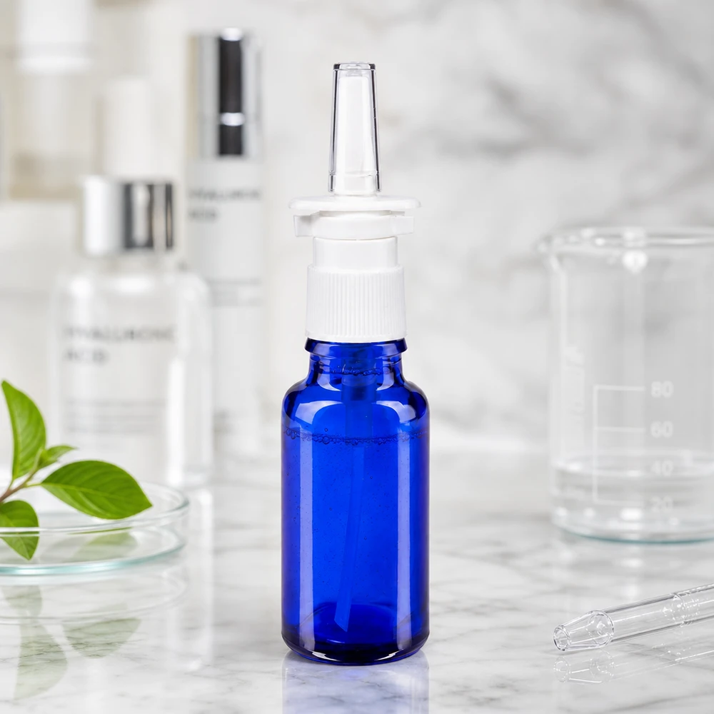 20 ml:n nenäsumutepullo sinisestä apteekkilasista, jossa on valkoinen sumutin, lasimaljan ja hyaluronihapon vieressä