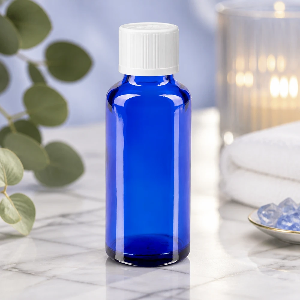 Sininen apteekkipullo (30 ml), jossa on valkoinen kierrekorkki, valkoisella marmorilla kristallien ja kynttilän vieressä