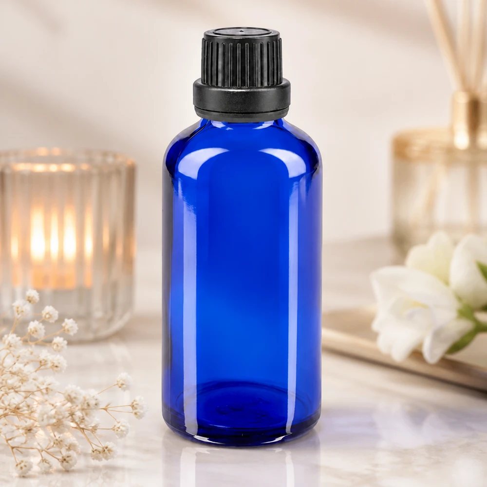 Apteekkipullo sininen 50ml tiputuskorkki valurengas 2mm musta peukaloinninesto suljin Koboltinsininen 50 ml:n lasipullo, jossa on musta kierrekorkki ja tiputusosa, kynttilän ja kukkien vieressä