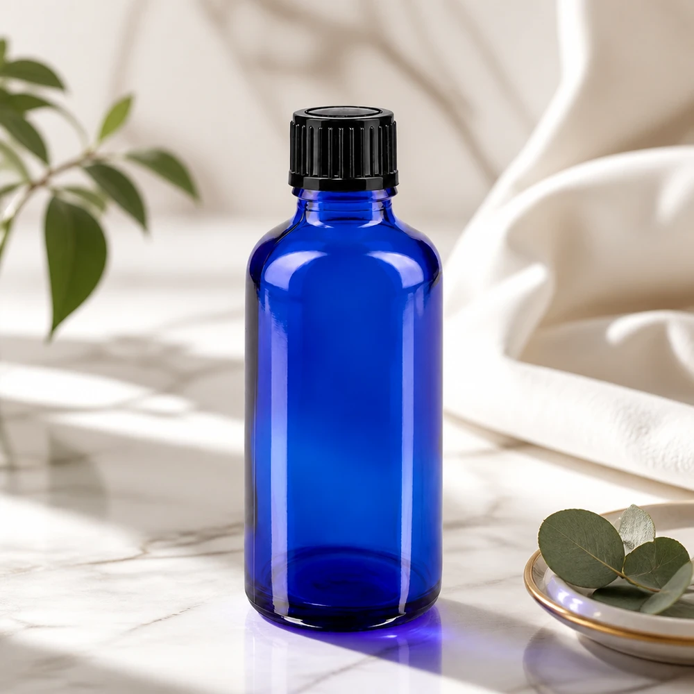 Sininen 50 ml:n lasipullo, jossa on musta korkki, marmorilla eukalyptuslehtien vieressä