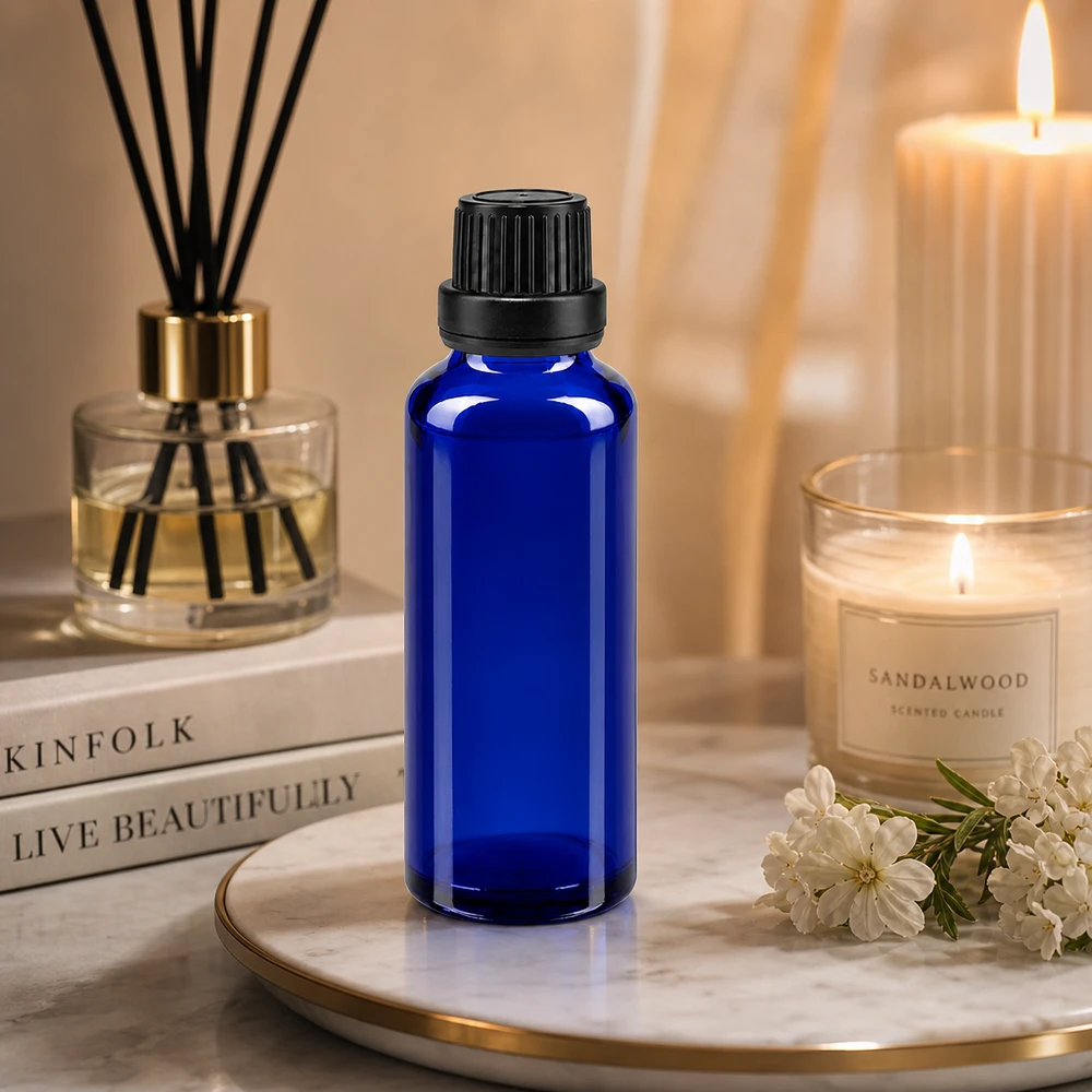 Apteekkipullo sininen 30ml tiputuskorkki kaaderengas 2mm musta peukaloinninestokorkki 30 ml:n sininen lasipullo, jossa on musta OV-korkki, marmorialustalla santelipuu-kynttilän ja diffuusorin vieressä