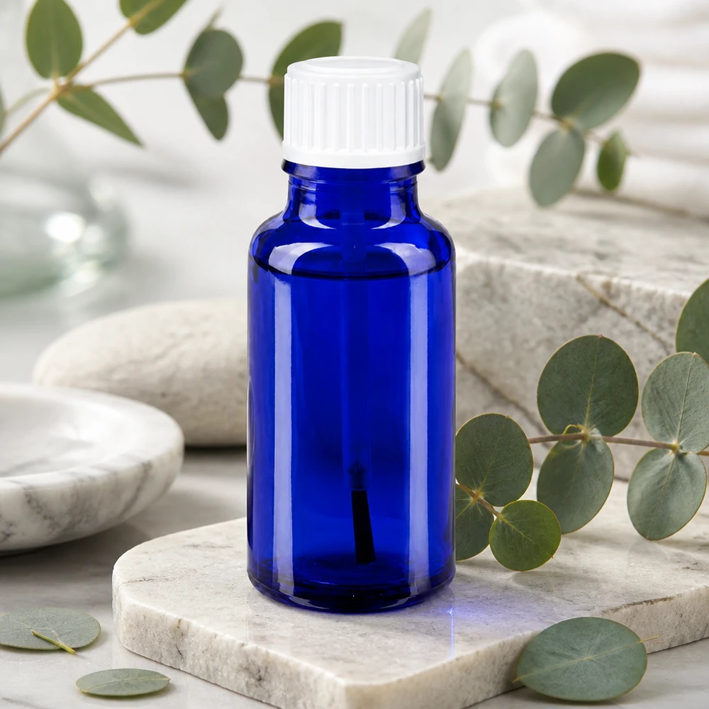 Apteekkipullo sininen 20ml ruuvikorkki valkoinen sivellinlaite Koboltinsininen 20 ml:n lasipullo, jossa on valkoinen sivellinpää, marmorin ja eukalyptuksen taustalla