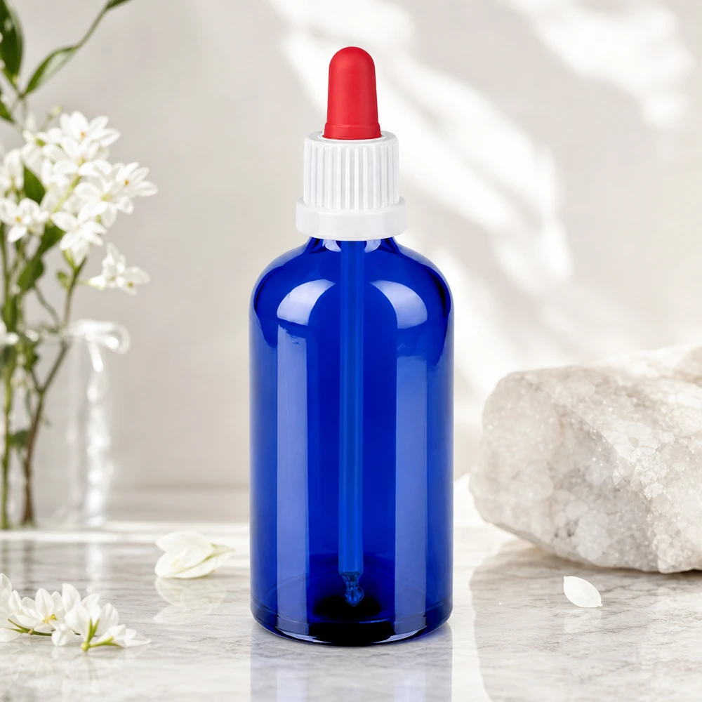 Tyylikäs sininen lasipullo 100ml, jossa on valkoinen kierrekorkki ja punainen pipetti eteerisille öljyille.