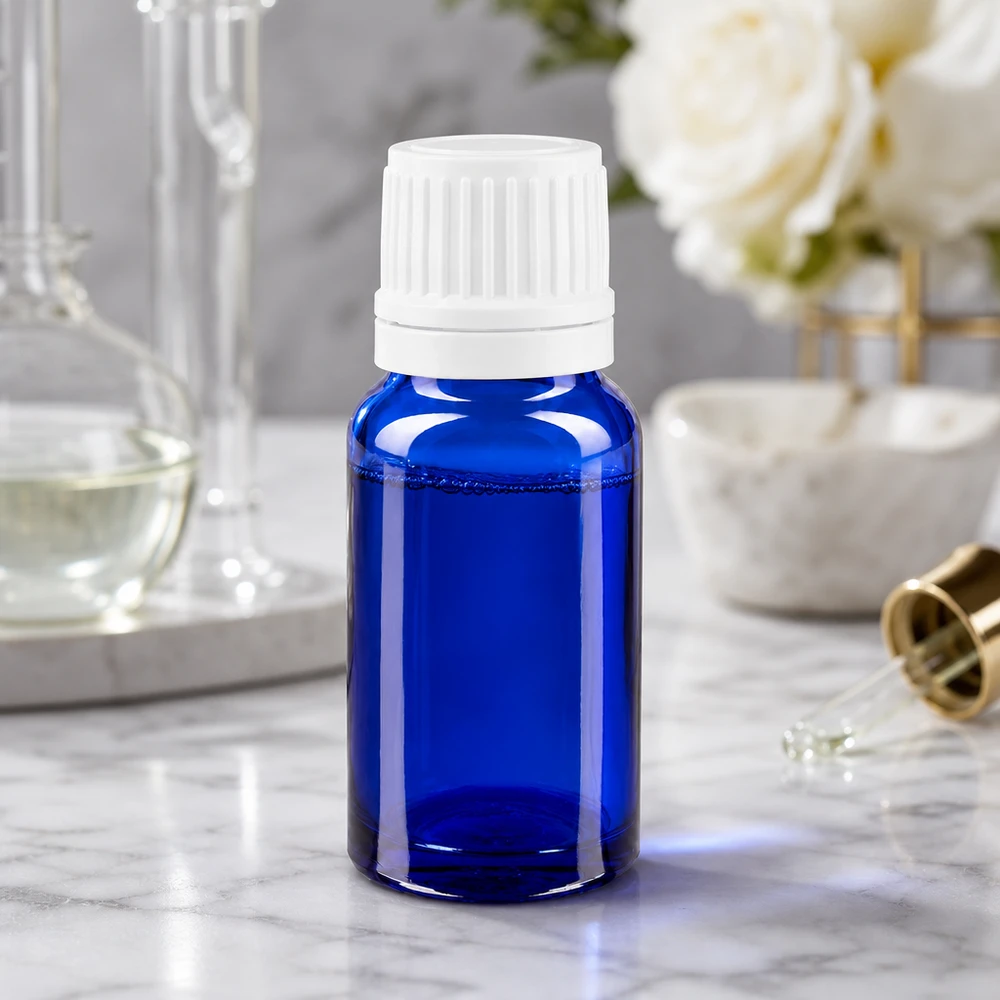 Apteekkipullo sininen 10ml tiputuskorkki 1.2mm valkoinen peukalointiturvallinen korkki 10 ml:n apteekkipullo, sinistä lasia, valkoisella tippakorkilla, marmoripinnalla ruusujen vieressä