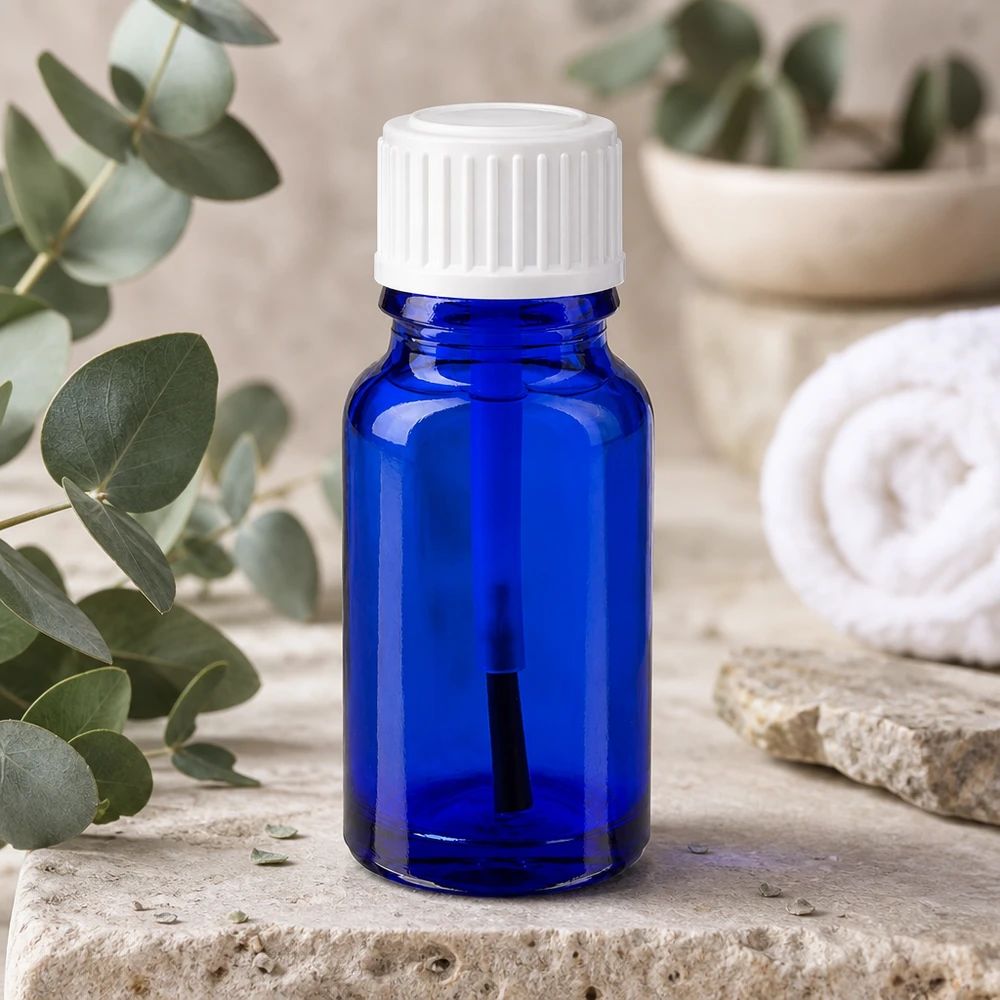 Apteekkipullo sininen 10ml ruuvikorkki valkoinen sivellin Sininen 10 ml:n lasipullo, jossa on valkoinen sivellinkärki, eukalyptusoksien vieressä luonnonkivellä