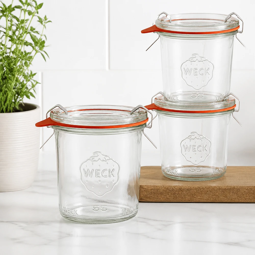 140 ml:n tumppupurkki täydellisenä WECK RR60 Kolme WECK 140ml RR60 -mukia pinottuna puiselle laudalle modernissa keittiössä, jossa taustalla on vihreä kasvi.