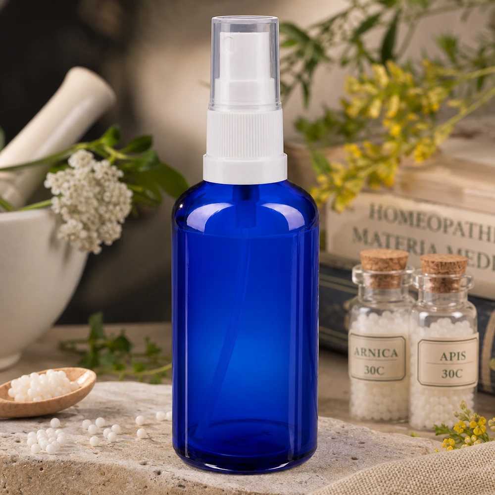 50 ml:n sininen apteekkilasinen suihkepullo, jossa on valkoinen pumppupää, homeopaattisten globulien vieressä